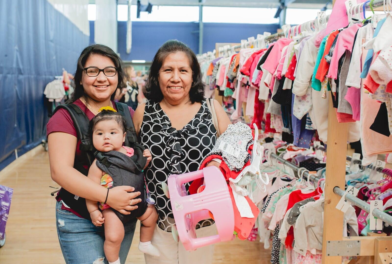 A mom, abuela and granddaughter attend a JBF sale. Abuela is holding a babyseat.