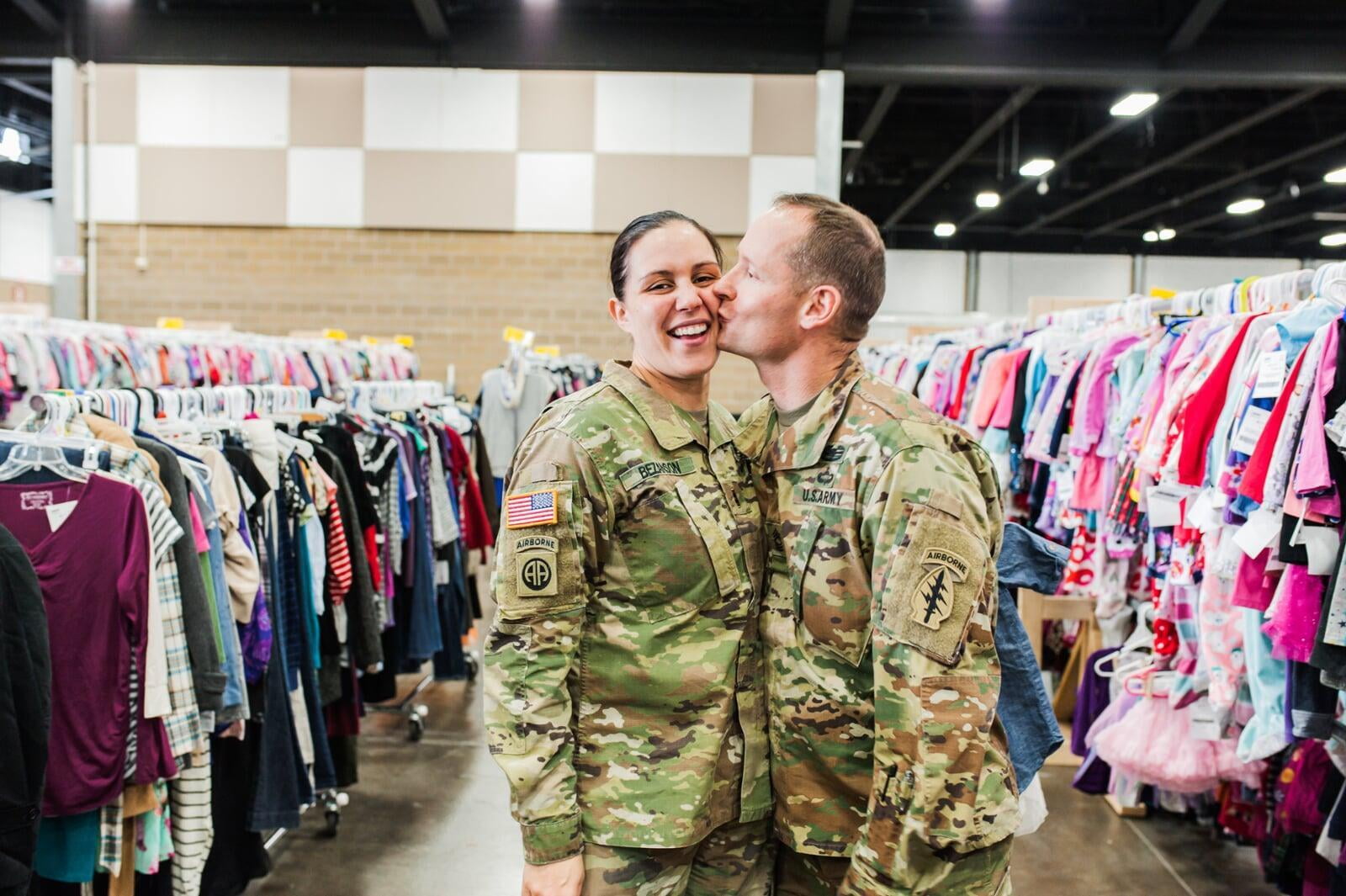 A military husband in camo kisses his military wife, also in camo, at the JBF sale.